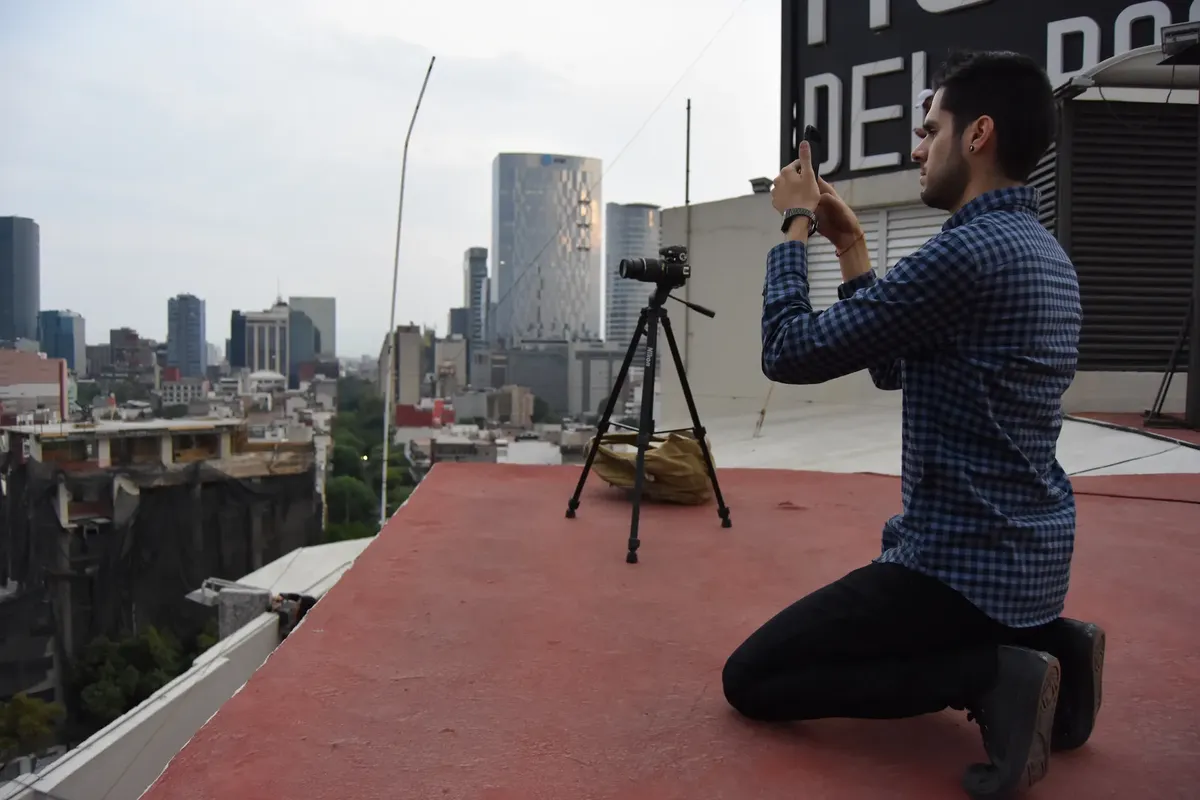 A photographer on a rooftop in Mexico City taking a photo of the skyline with a tripod and camera.