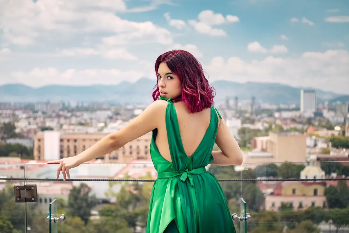Fashionable woman with pink hair in a green dress posing on a rooftop in Mexico City.