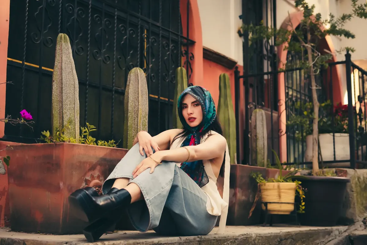 Fashionable young woman poses with cacti backdrop, showcasing street style.
