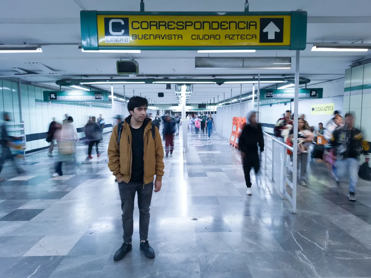 若者はメキシコ市内鉄道駅の忙しい通路の中にある。都市生活と人間の存在が融合している。